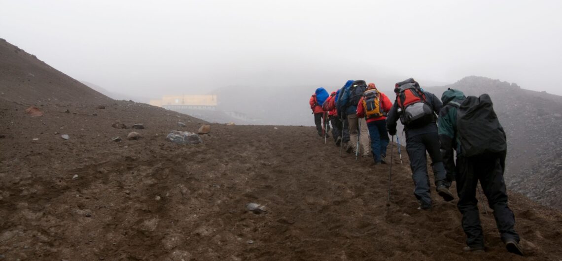 Group of hikers standing near the refuge hut on Cotopaxi Volcano, surrounded by mist and volcanic terrain