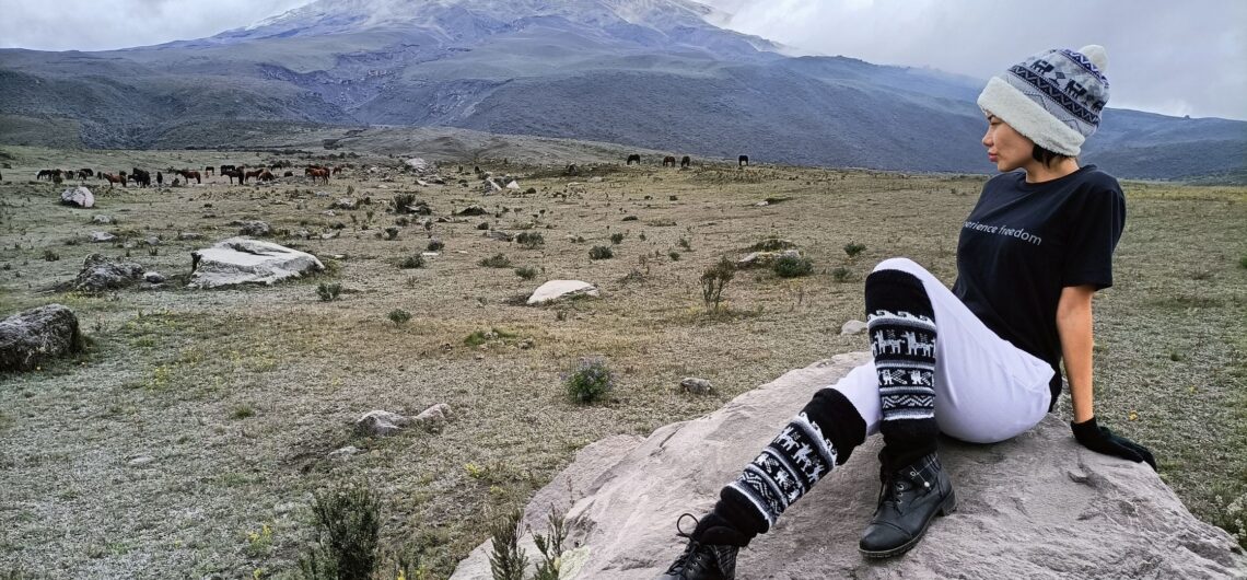 Traveler posing with a Barefoot Expeditions T-shirt in front of Cotopaxi Volcano, embodying the spirit of adventure and freedom