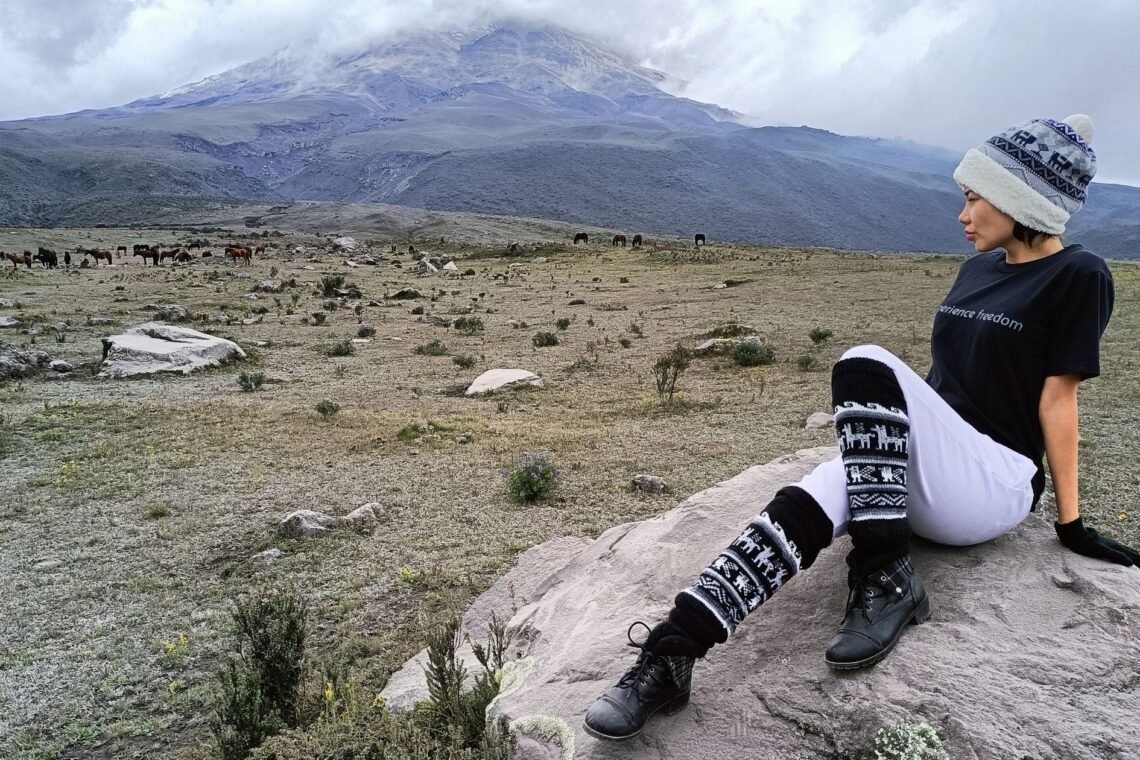 Traveler posing with a Barefoot Expeditions T-shirt in front of Cotopaxi Volcano, embodying the spirit of adventure and freedom